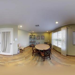 A cozy dining room with a round table, wooden chairs, and natural light streaming through large windows.