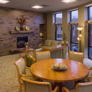 A cozy living room with a round table and chairs, featuring a fireplace and large windows.