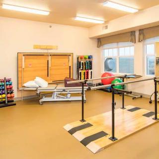 A well-equipped physical therapy room with parallel bars and various exercise tools.