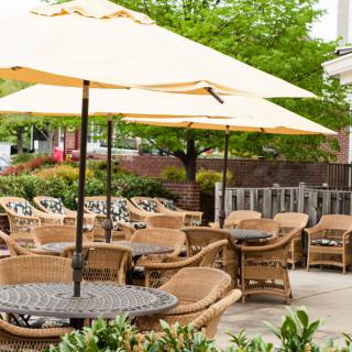 A peaceful outdoor patio area with wicker chairs and tables under large umbrellas, surrounded by greenery.