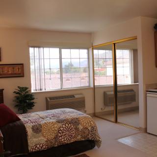 A cozy bedroom interior with a bed, large windows, and mirrored closet doors.