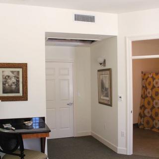 A hotel room interior with a desk, wall artwork, and open doorways.