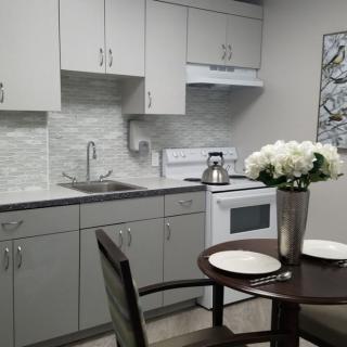 A modern kitchen with white cabinets, a small dining area, and decorative flowers.