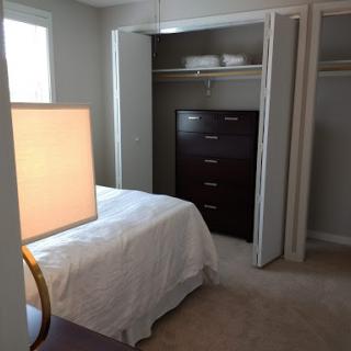 A cozy bedroom featuring a neatly made bed, a stylish lamp, and ample storage space with a dresser and closet.