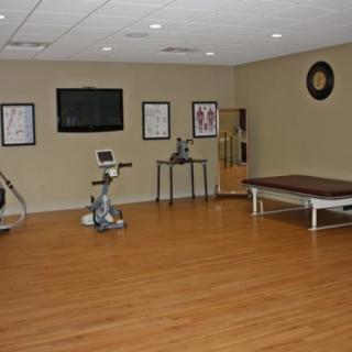 A spacious gym or therapy room with various exercise equipment and a treatment table.