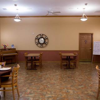 An empty dining room with wooden tables and chairs, adorned with a large wall clock.