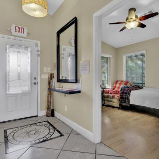 A cozy interior view featuring a welcoming entrance, a mirror on the wall, and a glimpse into a bedroom with a ceiling fan and sunlight streaming through the windows.