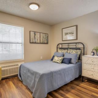 A cozy bedroom with a neatly made bed, artwork on the walls, and hardwood flooring.