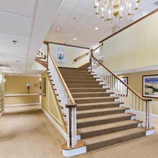 A spacious lobby featuring a grand staircase with railings, adorned by a chandelier and artwork on the walls.