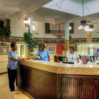 Hospital reception area with staff assisting a visitor.