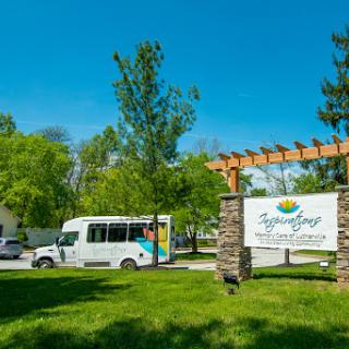 A bus parked in front of a welcoming sign among lush greenery and under a clear blue sky.