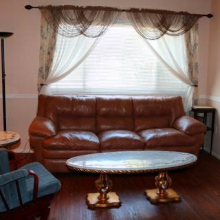 A cozy living room with a brown leather sofa, an oval coffee table, and elegant curtains.