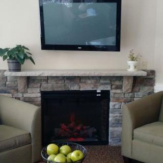 A cozy living room setup with a stone fireplace, TV, armchairs, and a bowl of apples on the coffee table.