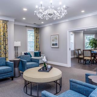 A modern and cozy living room with blue chairs, a chandelier, and a round table.