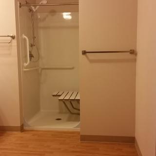 An accessible bathroom with a shower featuring grab bars and a foldable seat.