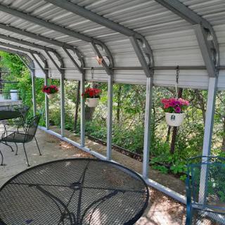 A serene outdoor patio area adorned with colorful hanging plants and ample seating, surrounded by lush greenery.