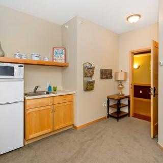 A cozy kitchenette in an apartment with a mini fridge, microwave, and wooden cabinetry.