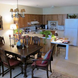 A cozy dining area connected to a kitchen, featuring a wooden table and chairs, with plants and decorative items adorning the space.