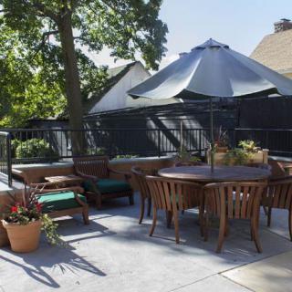 A cozy outdoor patio with wooden furniture and a large umbrella, surrounded by potted plants.