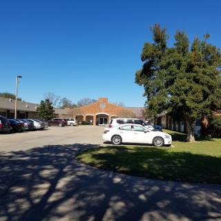 A sunny day at a parking area near a building, with a white car parked on the grass.