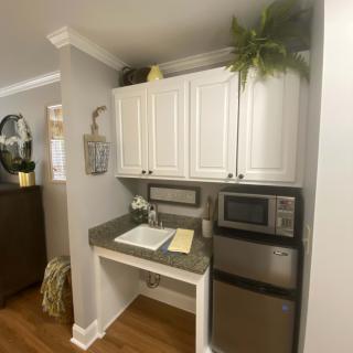 A cozy kitchen nook featuring white cabinets, a microwave, a compact fridge, and decorative plants.