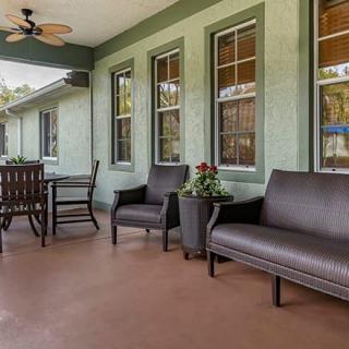 A cozy porch area featuring outdoor seating with chairs and a table, complemented by a ceiling fan and potted plants.