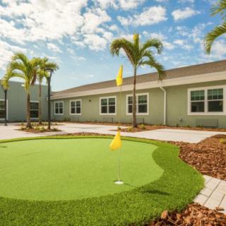 A sunny courtyard with a small putting green surrounded by palm trees and a building.