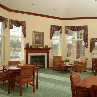 A cozy living room with tables, chairs, and a fireplace surrounded by large windows.