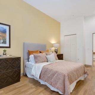 A cozy bedroom featuring a neatly arranged bed with modern bedding, framed artwork on the wall, and stylish furnishings including dressers and a lamp.