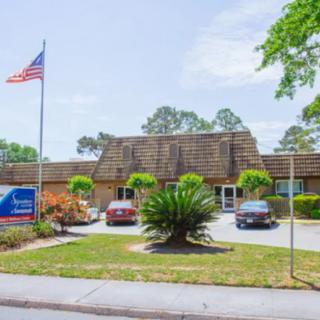 A building with an American flag, surrounded by trees and cars parked in the driveway.