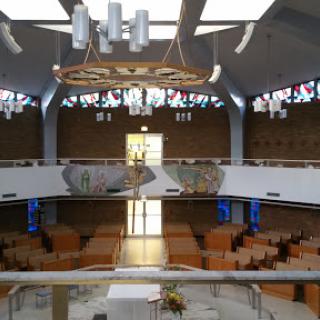 A modern church interior featuring wooden benches, decorative windows, and ample natural light.