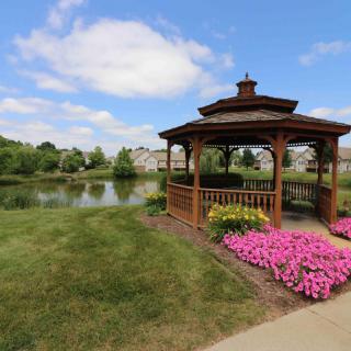 A scenic view of a wooden gazebo by a lake with colorful flowers in a park.