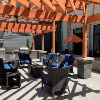 A modern outdoor patio area with a wooden pergola, featuring comfortable seating and blue-cushioned chairs.