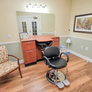 A cozy salon room featuring a barber chair, mirror, and comfortable seating.