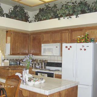 A cozy kitchen with wooden cabinets, white appliances, and decorative greenery on top of the cabinets.
