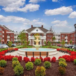 A beautiful landscaped area with a central fountain in front of a grand building, surrounded by vibrant flowers and greenery.