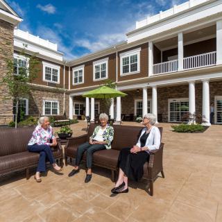 Three seniors enjoying a conversation on the patio of a retirement home.
