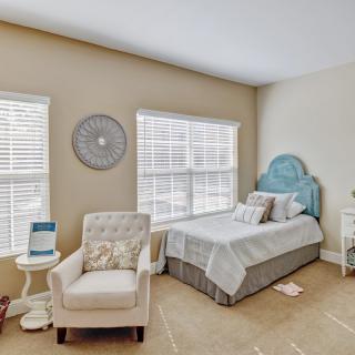 A cozy bedroom with a single bed, armchair, and two large windows letting in natural light.