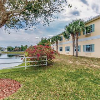 A serene lakeside view with a building, surrounded by lush greenery and palm trees.