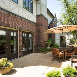 A cozy outdoor patio with furniture and an umbrella on a sunny day beside a brick building.