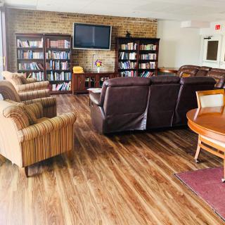 A cozy library seating area with leather sofas and armchairs, surrounded by bookshelves and a TV.