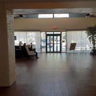 A spacious lobby with natural lighting, featuring a seating area and entrance doors.