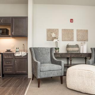A cozy living space with modern decor, featuring a kitchenette, armchairs, and a small dining table.