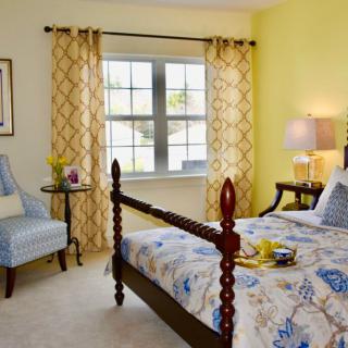 A cozy bedroom with a classic wooden bed, patterned bedding, and bright yellow walls.