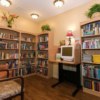 A cozy library corner with bookshelves, a computer, and decorative plants.