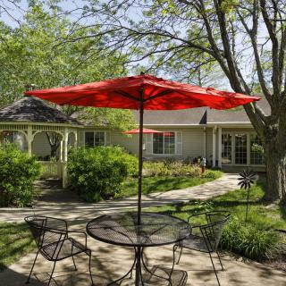 A peaceful garden patio with a red umbrella and metal furniture on a sunny day.