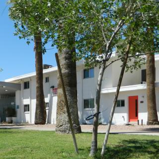 A modern residential building with white walls, red doors, and surrounded by trees on a sunny day.