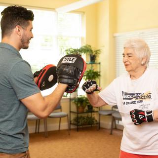 An elderly woman is training in boxing with a coach indoors.