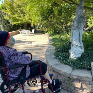 An elderly person enjoying a serene moment in a garden, observing a statue.