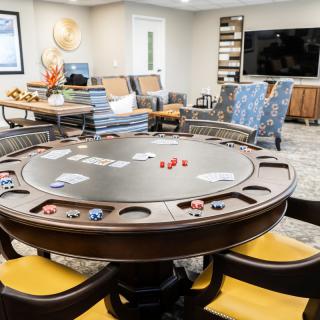 A modern game room featuring a poker table with cards and chips, surrounded by comfortable seating and a large television.